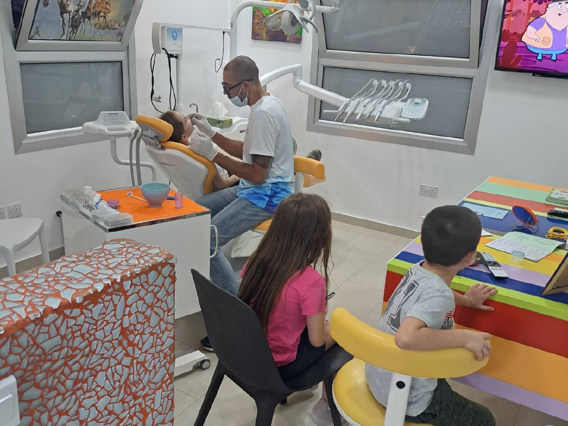 Dr. Yanik treating a child while their siblings cheerfully watch cartoons waiting for their appointment.